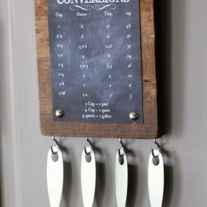 Finished kitchen conversion chart displayed on the refrigerator with four measuring spoons hanging underneath.