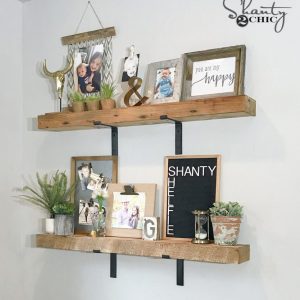 Two DIY chunky wood shelves mounted on a white wall with black industrial brackets and styled with framed photos, plants, and decor.