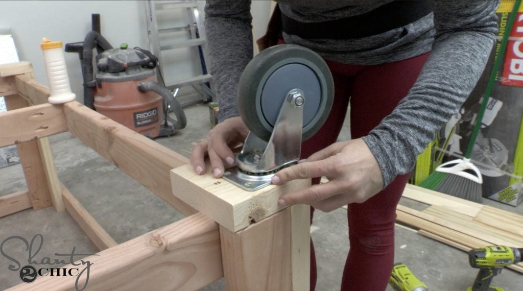 Positioning a caster on the wood foot pad underneath the rolling workbench.