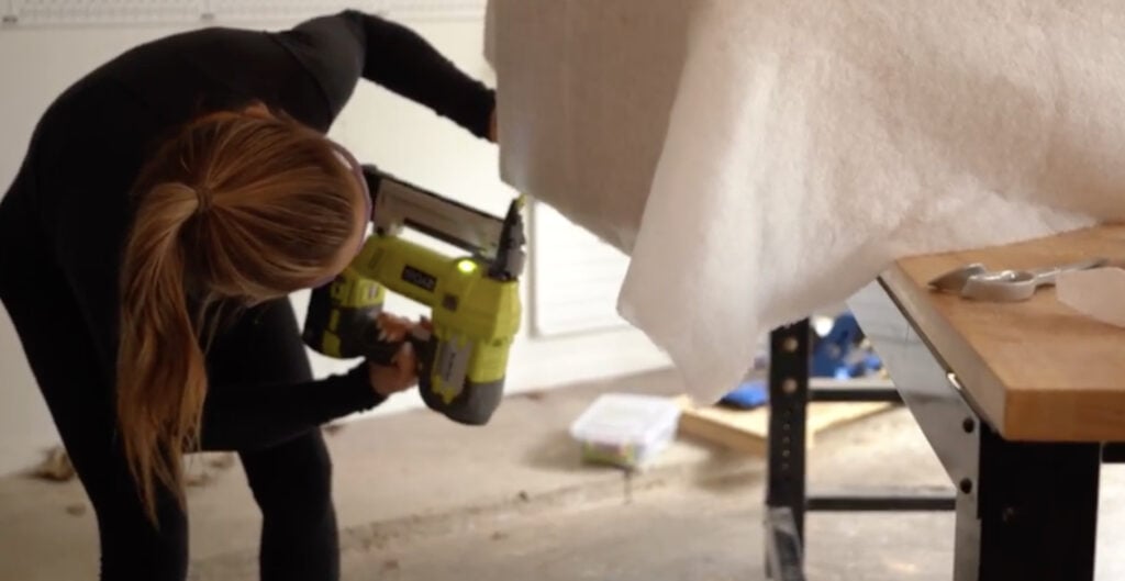 Tacking batting to the bottom edge of the plywood sides before upholstering the bench.