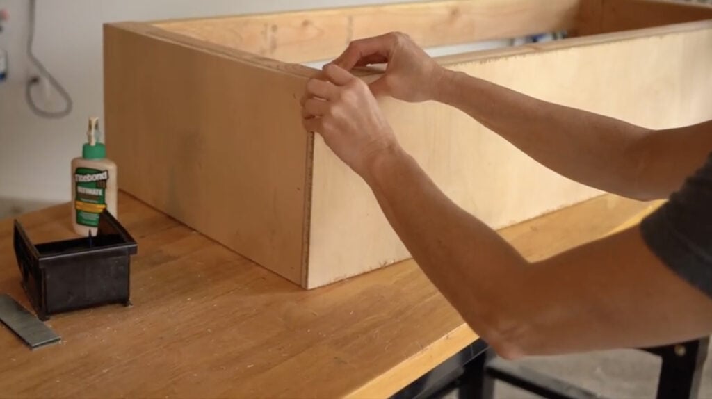 Attaching the front plywood panel to the DIY cowhide bench frame.