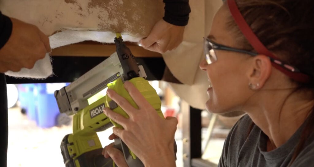 Stapling the cowhide upholstery to the underside of the DIY bench frame.