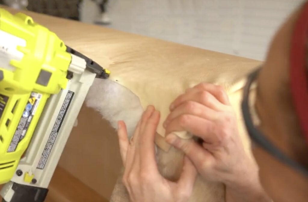 Securing the folded cowhide corner to the bottom edge of the plywood.